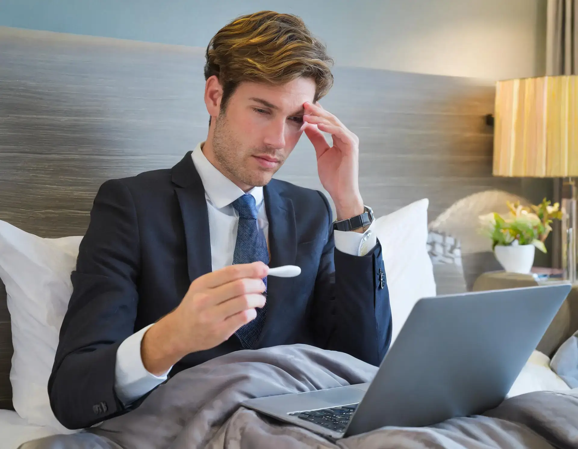 young businessman wearing suit in bed checking his temperature
