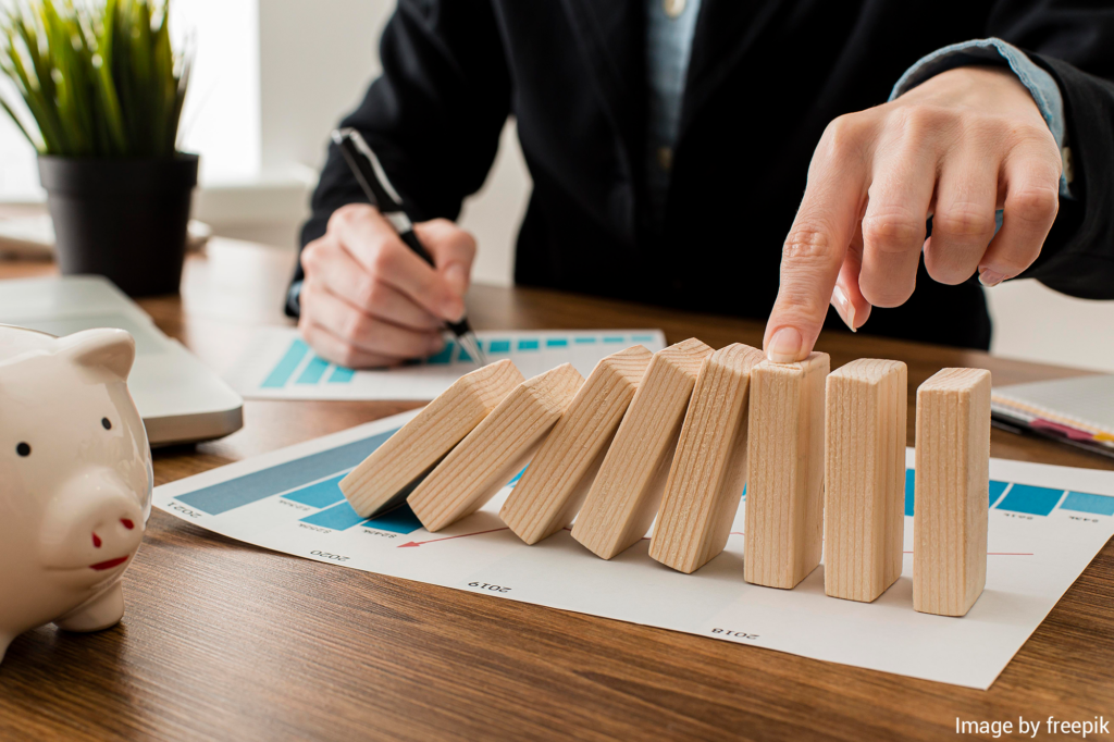 business man looking reviewing charts and holding wooden domino blocks in place to avoid them toppling