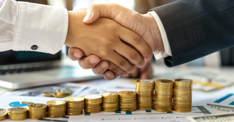 Businesspeople shaking hands over increasing stacks of coins and financial documents