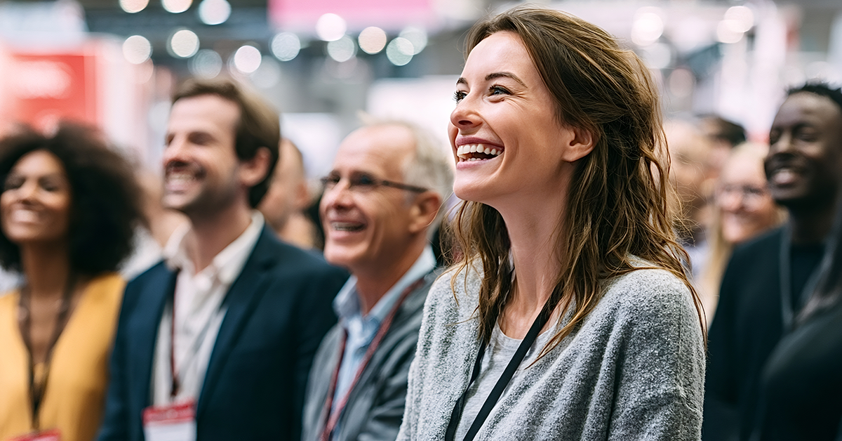 Diverse group of business people, including a smiling woman in the foreground, attending a professional conference or event, actively engaging and finding amusement in the presentation